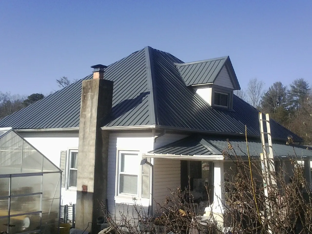 Dark blue standing seam metal roof on a white farmhouse with dormer — Slate & Tile Roof Repair by Roofing Brothers in Vardaman