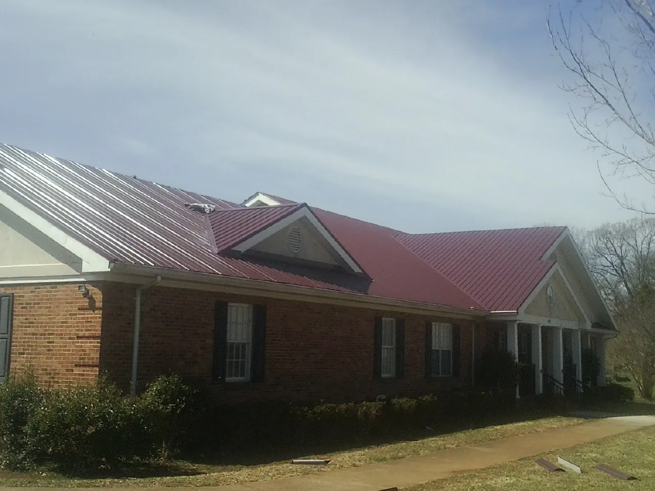 Red metal roof with gabled entries on a long brick building, from a Hail Damage Roof Repair job in Vardaman