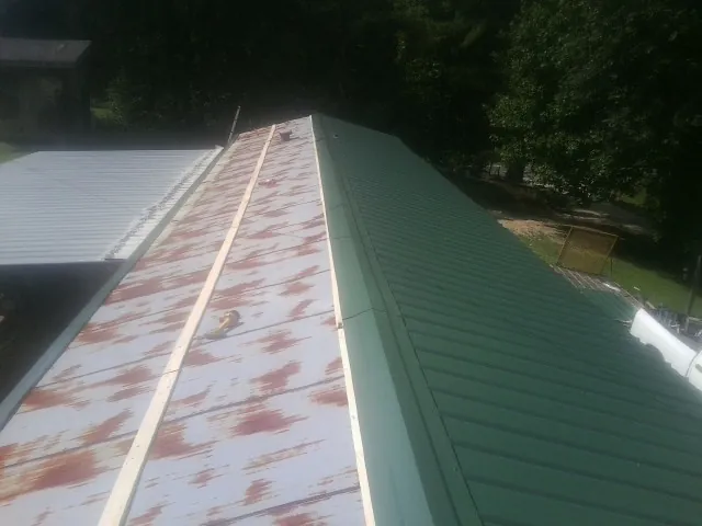 Old rusted panels beside newly installed green metal roofing — Wind Damage Roof Repair by Roofing Brothers in Vardaman