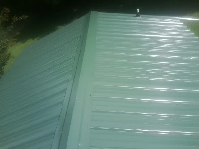 New green metal panels meeting at the ridge of a roof — Flat Roof Repair work by our crew in Vardaman