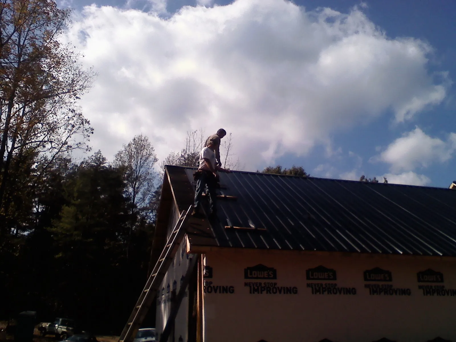 Roofer fastening dark metal panels high against a cloudy sky, from a Roof Inspection job in Vardaman